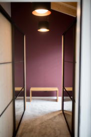 Stilvolle Ankleide mit Massivholz und modernen Kontrasten - Ankleidezimmer mit naturfarbener Holzbank, Spiegel-Schiebetüren und auberginefarbener Wand.