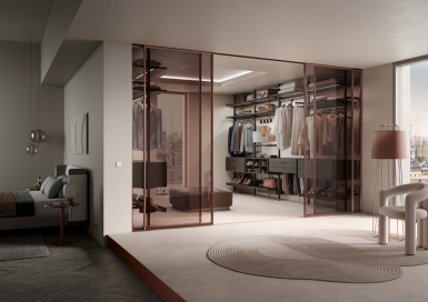 Raumplus Gleittüren - Eleganter Ankleidebereich mit maßgefertigten Gleittüren aus Glas und Metallrahmen von unserem Partner raumplus, verbunden mit einem modernen Schlafzimmer.
